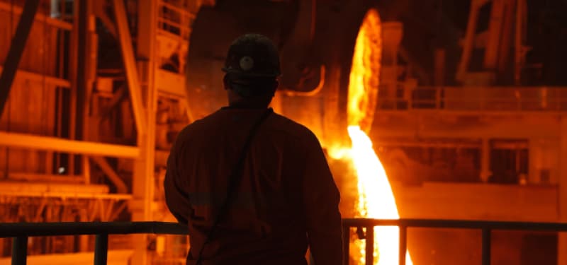 Man standing in front of molten metal being poured